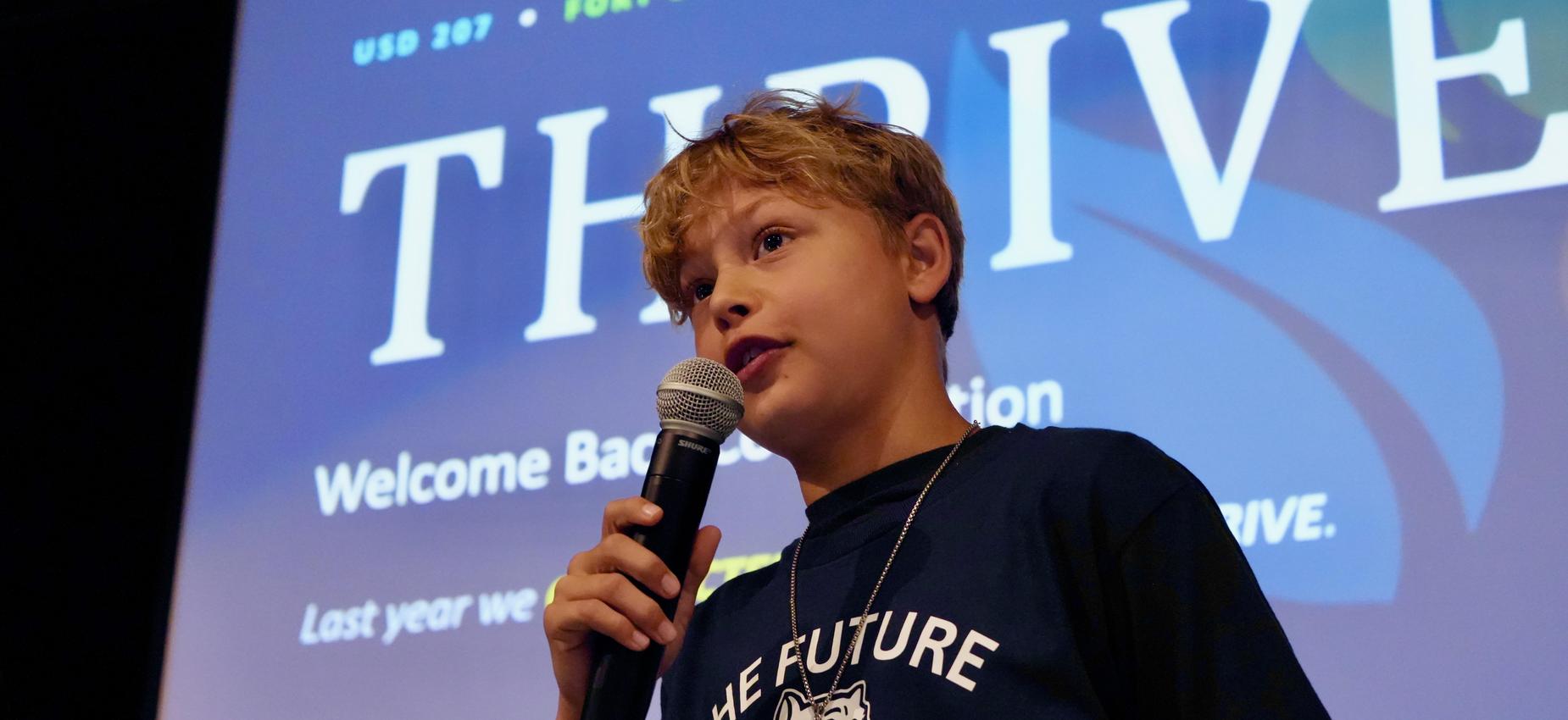 Boy speaking into a microphone on stage with a thrive backdrop.