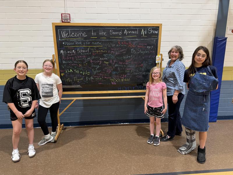student leaders and art teacher in front of sign welcoming families