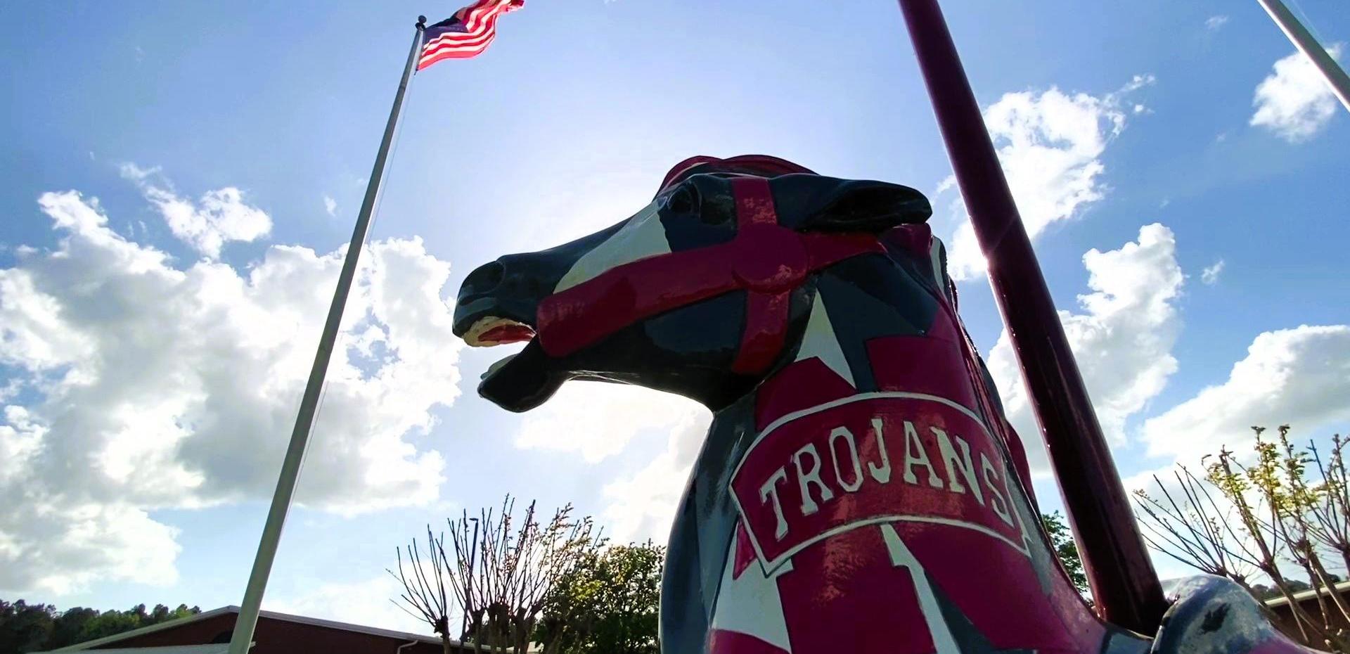Colorful Trojan mascot statue with an American flag and blue sky.