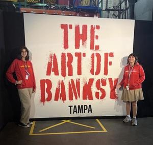 2 girls pose with "Art by Banksy" sign