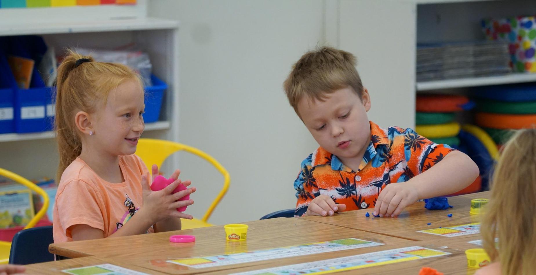Children playing with colorful play dough at a classroom table.