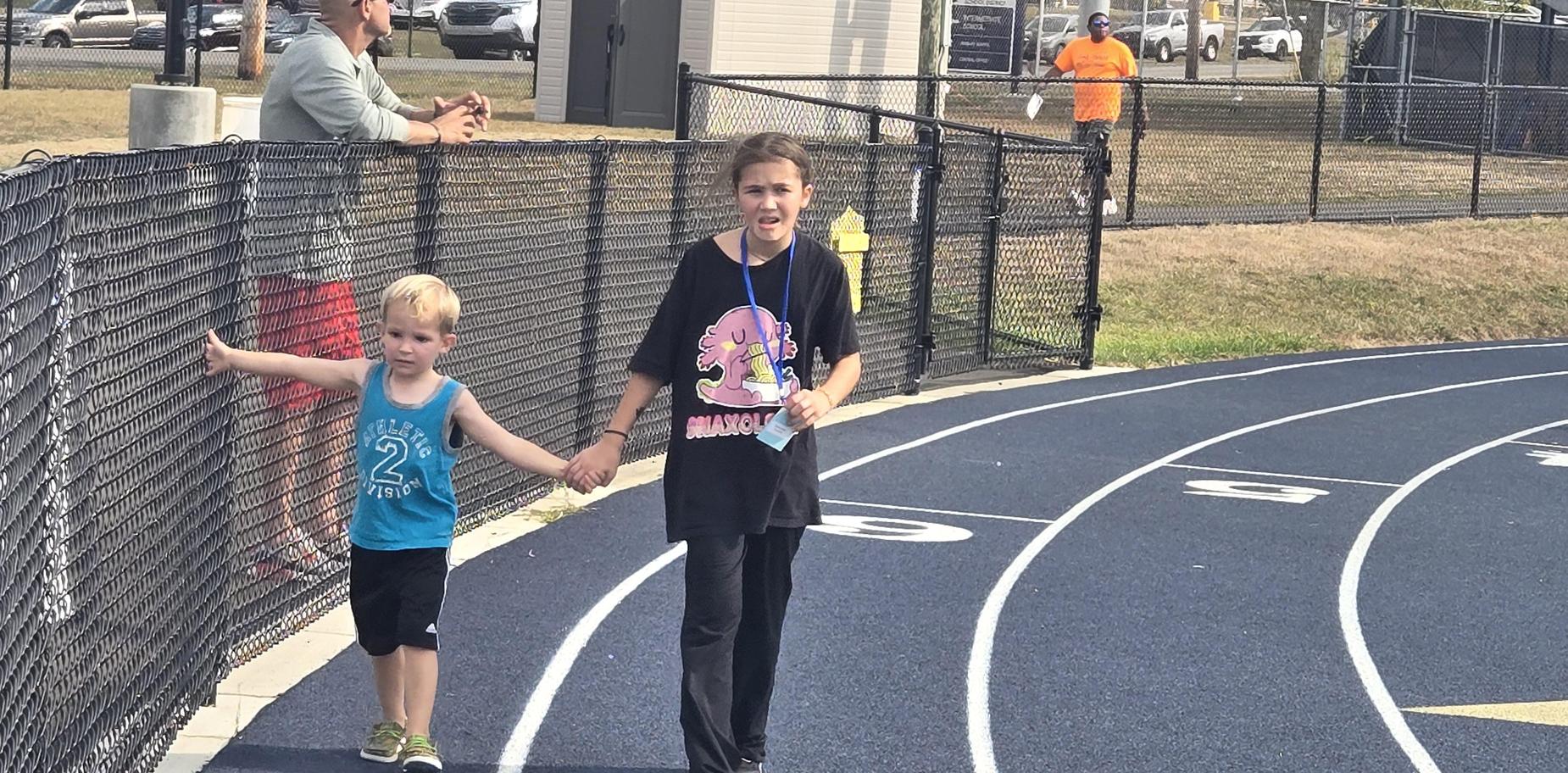A boy and a girl holding hands while strolling on the track with smiles on their faces.