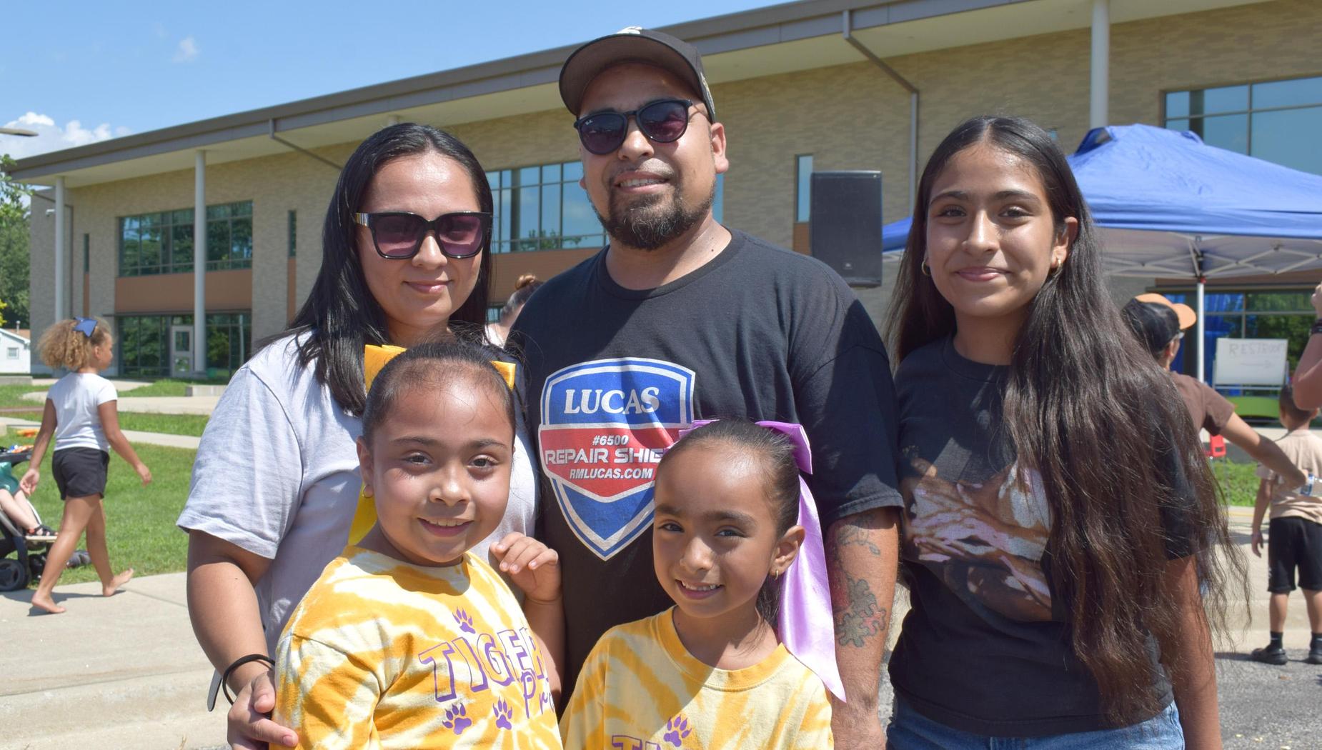 A family posing together, with two girls in tiger shirts and a man in a hat.