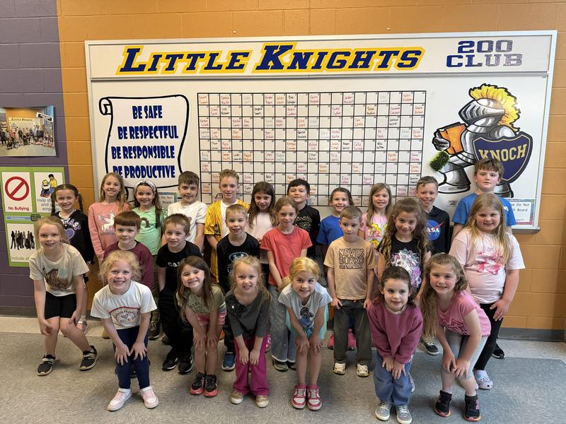 primary students smiling at camera in front of little knight board