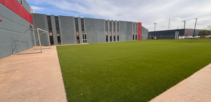 A green turf field in front of gray and red building