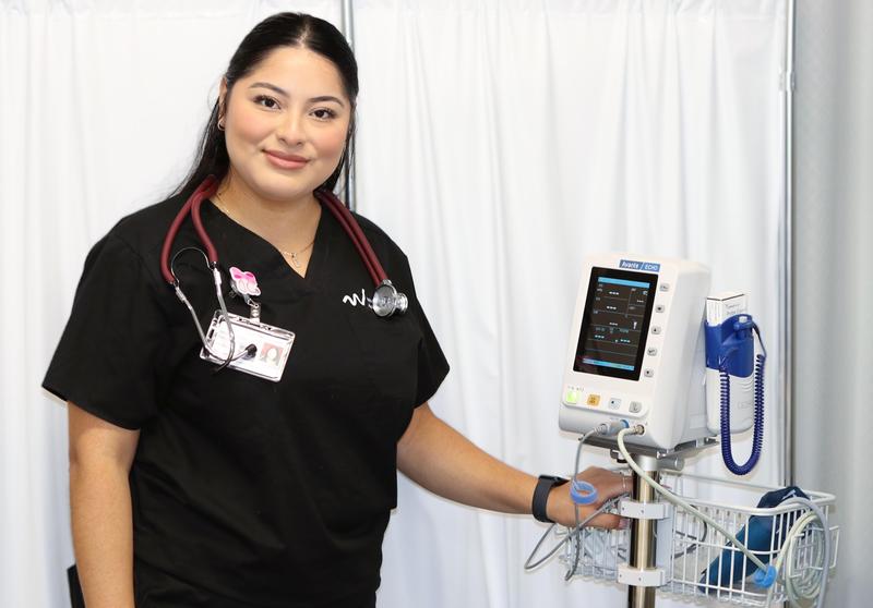 A female Whittier Union Adult School medical assistant student smiles while displaying her medical equipment.
