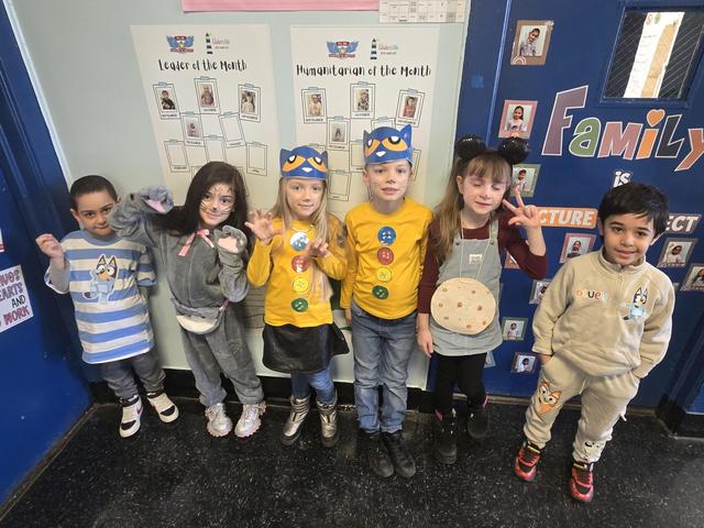 Group of children in colorful costumes posing together in a school hallway.