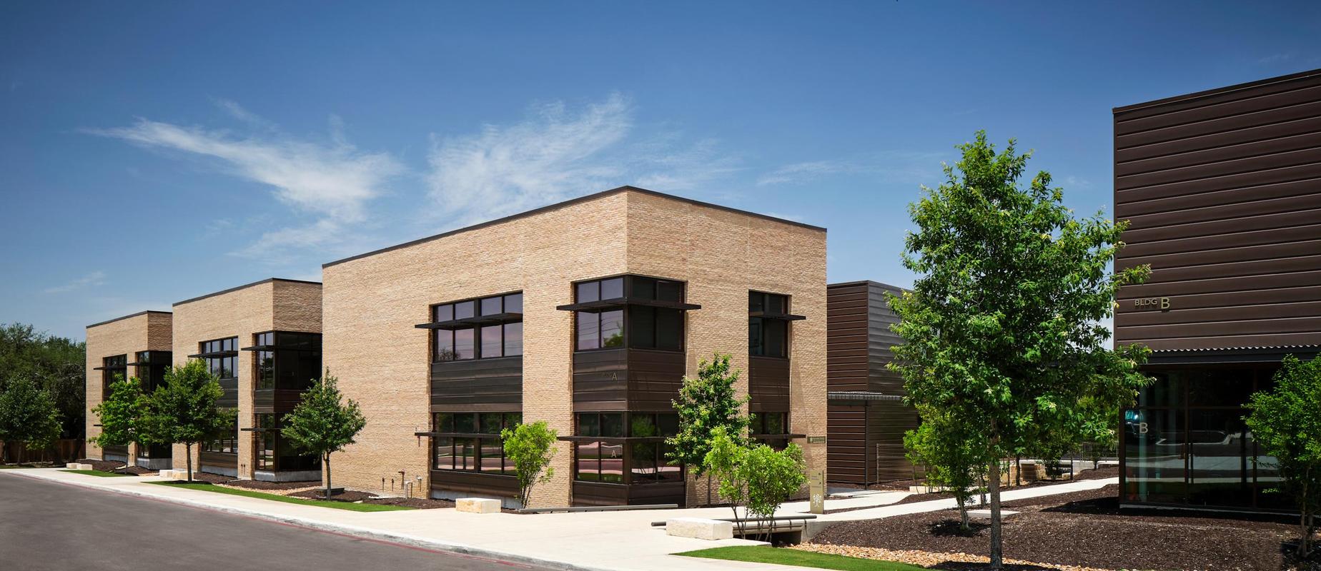 Modern brick buildings with large windows and trees lining the walkway.