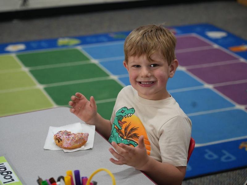 Smiling boy sitting at a table with a donut and art supplies in front of him.