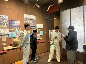 Four young people explore an exhibit with displays and artwork on the walls.