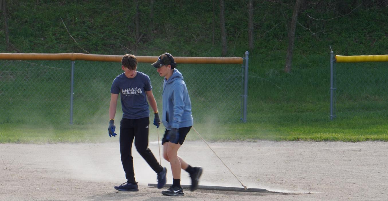 Two young people smoothing a dirt field with a board, creating a clean surface.