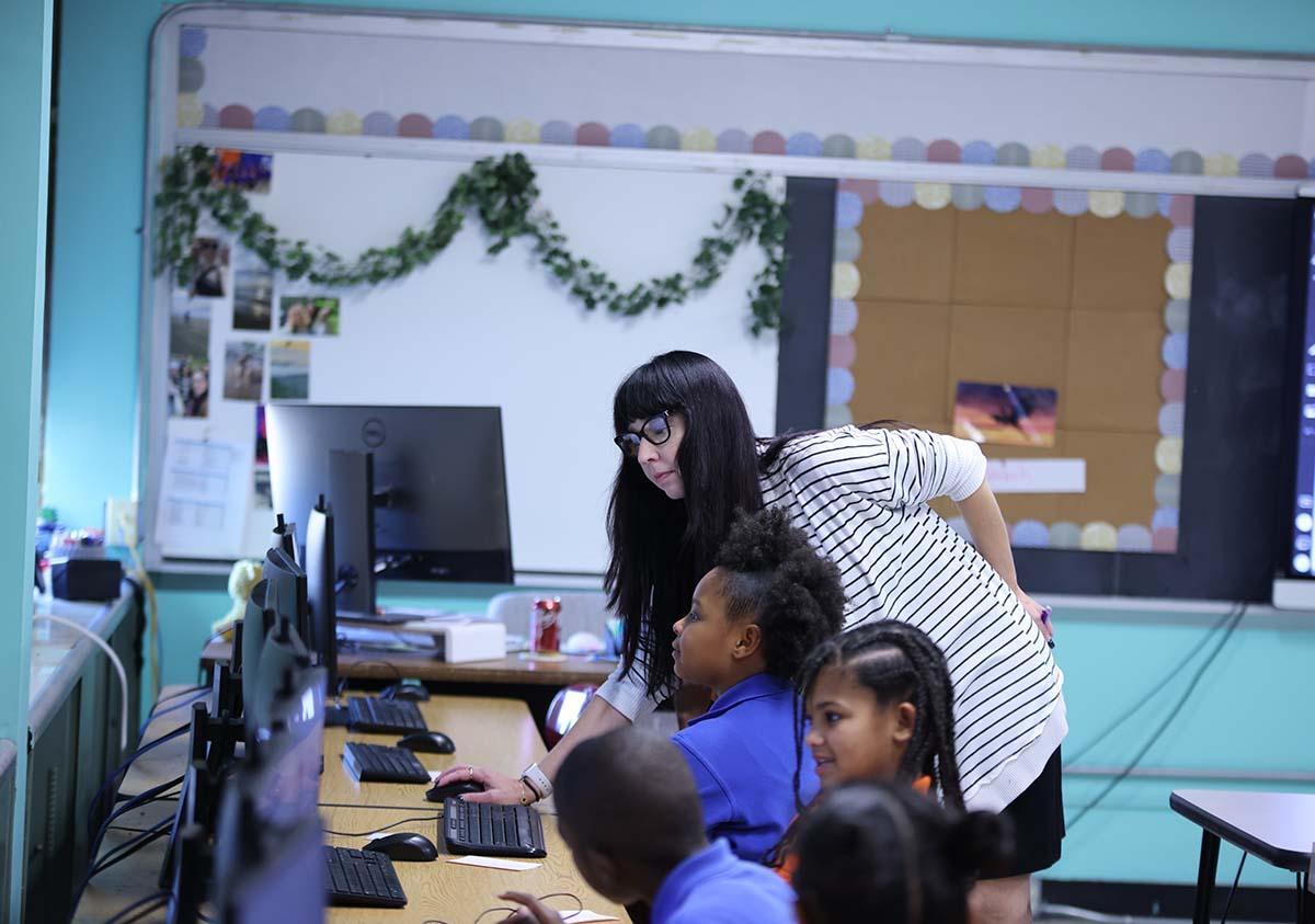HSA Teacher smiles while kneeling beside a young student in a classroom setting.
