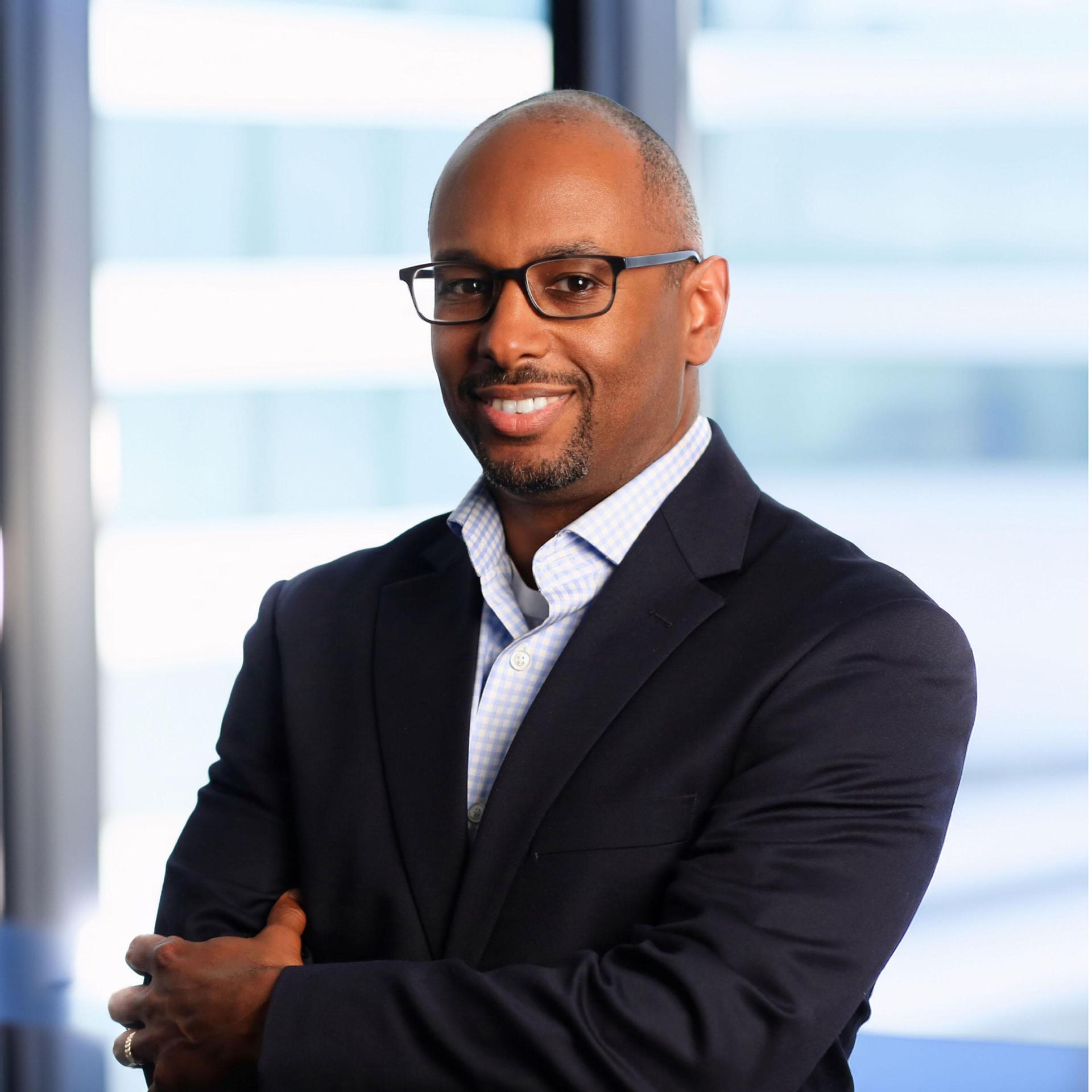 Mark Lewis in a suit and tie, standing with his arms folded