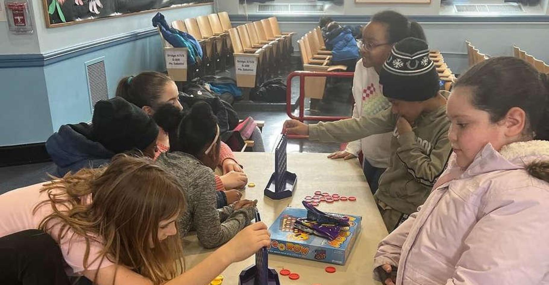 Children playing a tabletop game in a lively classroom setting.