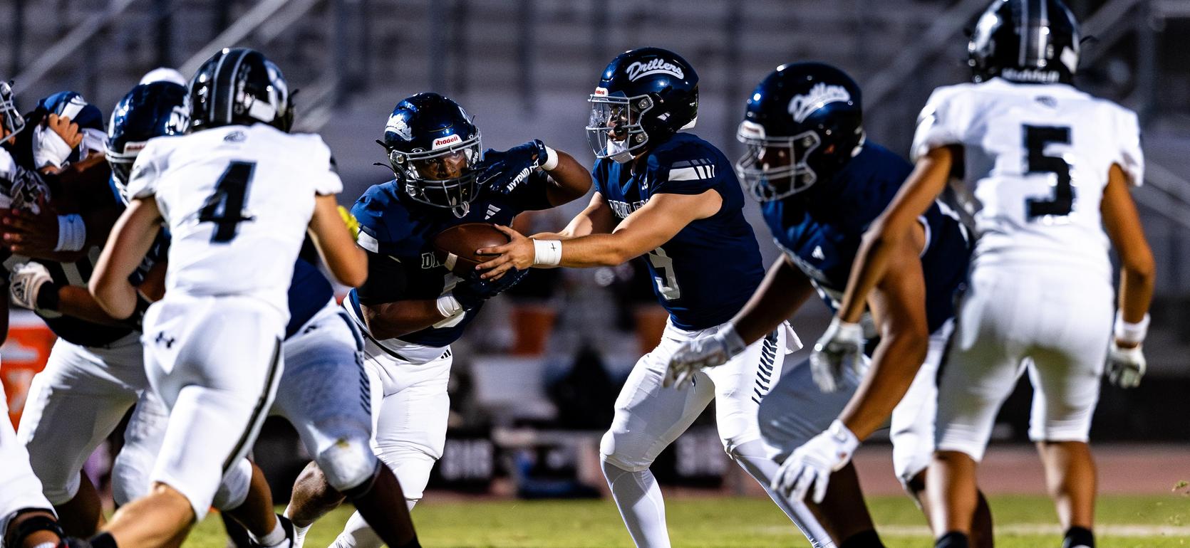 A football team in blue uniforms executing a play during a game against a team in white.