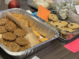 A tray of various cookies, including oatmeal and chocolate chip, with an apple nearby.