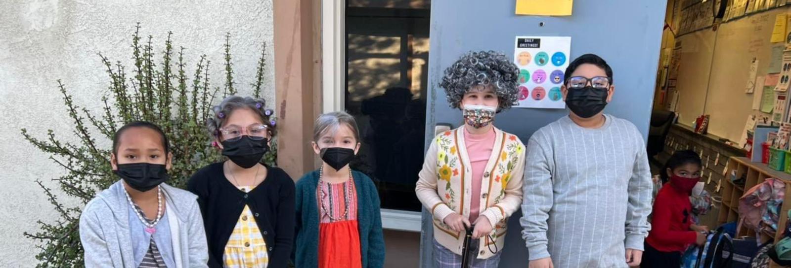 Students infront of classroom door celebrating 100 days in school wearing senior citizen costumes