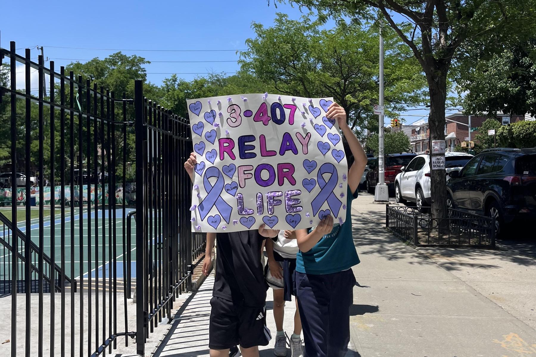 Children hold a colorful sign for Relay for Life with hearts and ribbons.