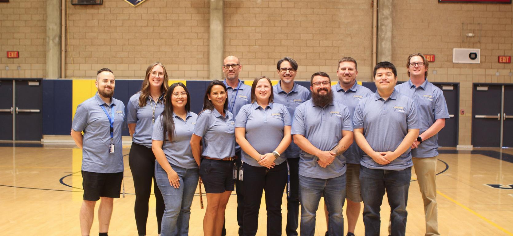 Group of staff members posing in blue shirts on a gym floor.