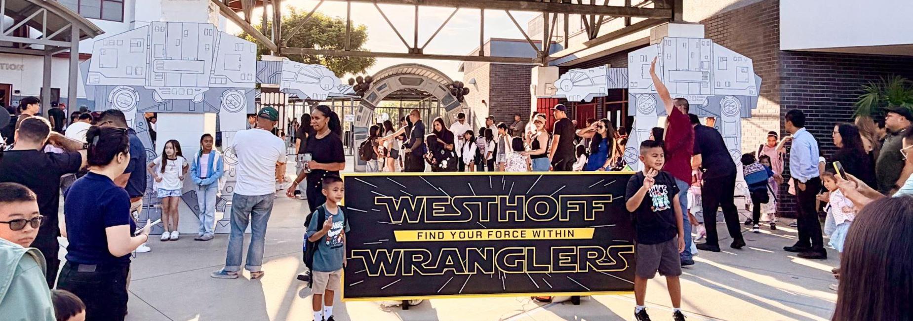 A busy outdoor event entrance with a large banner and crowds of people.