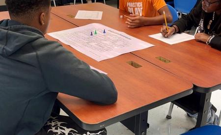 Students seated at a table, engaged in gameplay with a board and writing materials.