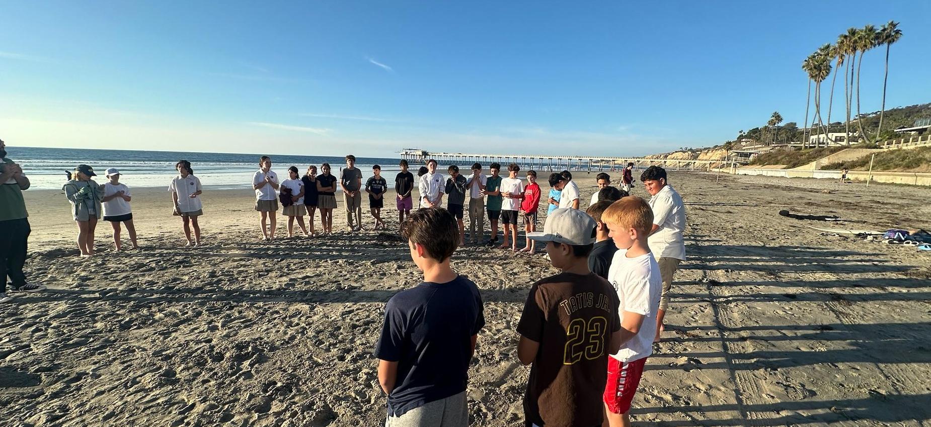 Students gathered in a circle at the beach before they do a beach clean up