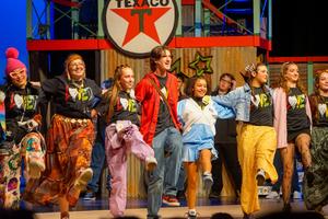 Cast of Godspell in a line, kicking their legs as a part of a musical number.