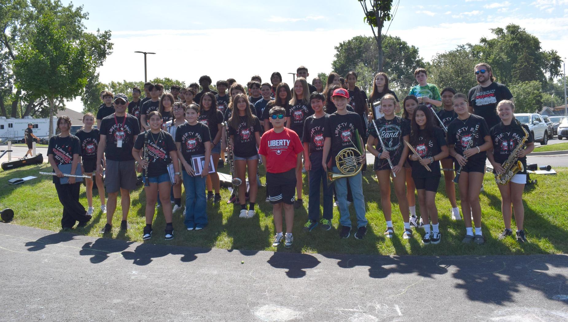 A large group of students with instruments posed together outdoors for a photo.