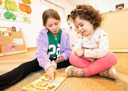 Two children of varying ages discussing a book