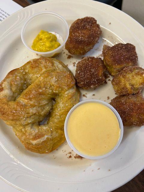 A plate with a soft pretzel, mustard, and sweet doughnut-like bites.