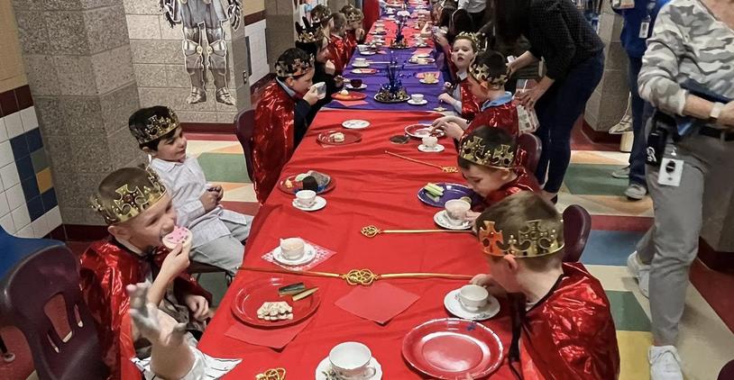 Children dressed as royalty enjoying a decorated feast at a long table.