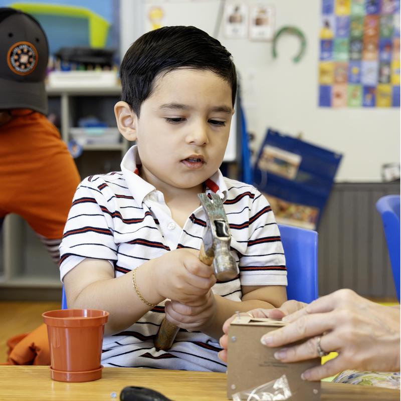 Child using a hammer to work on a craft project in a classroom.