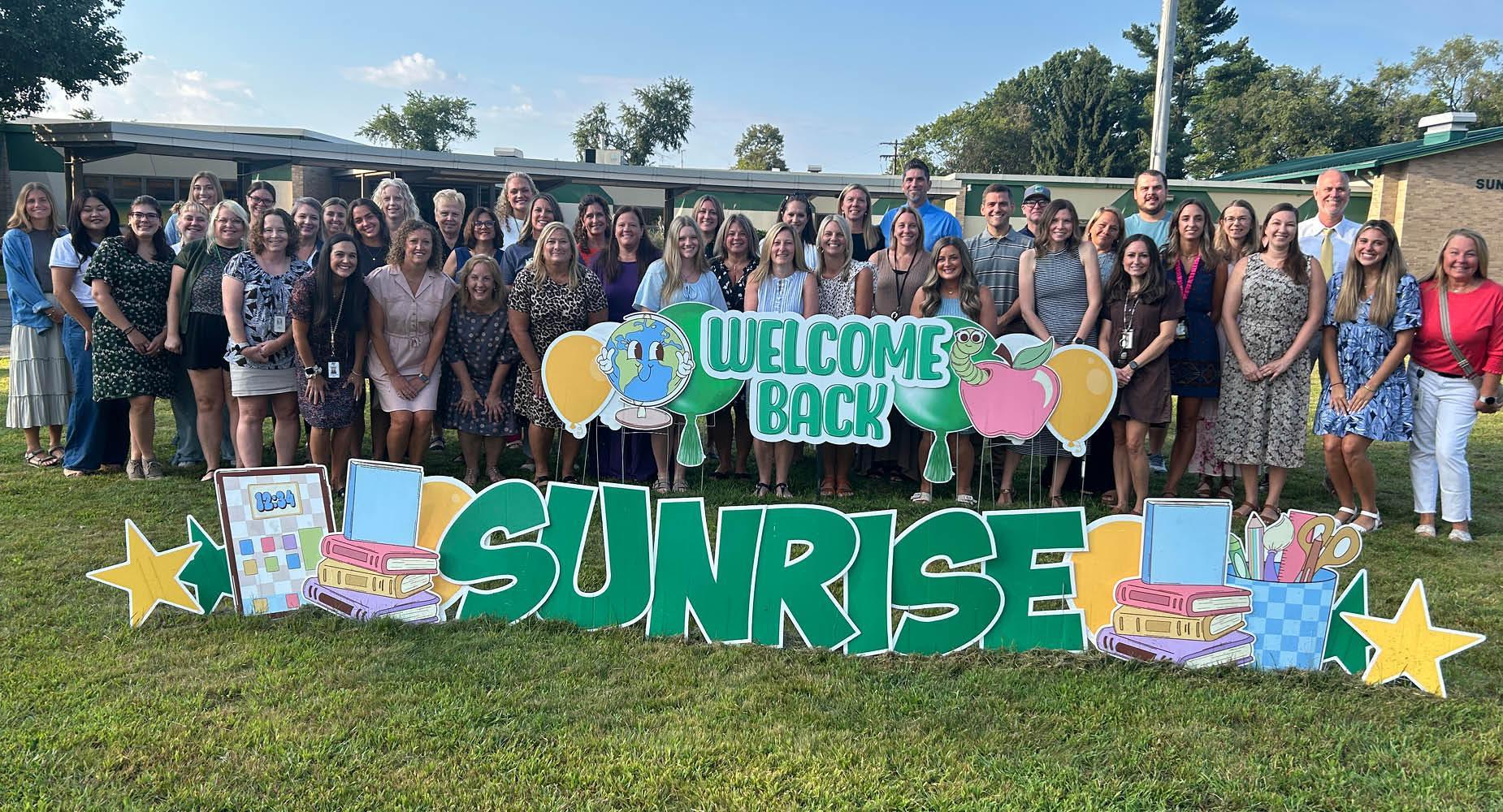 Group of teachers standing together in front of a welcome back sign.
