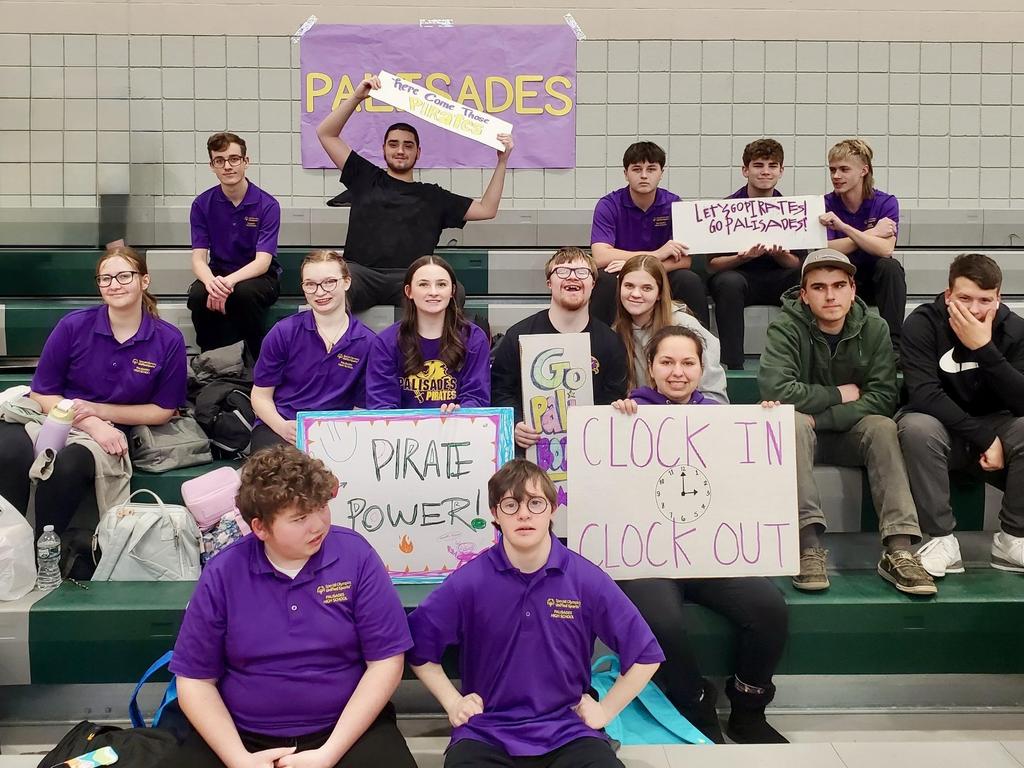 Students in the bleachers holding signs to support the Pirates competing in a Unified sporting event.