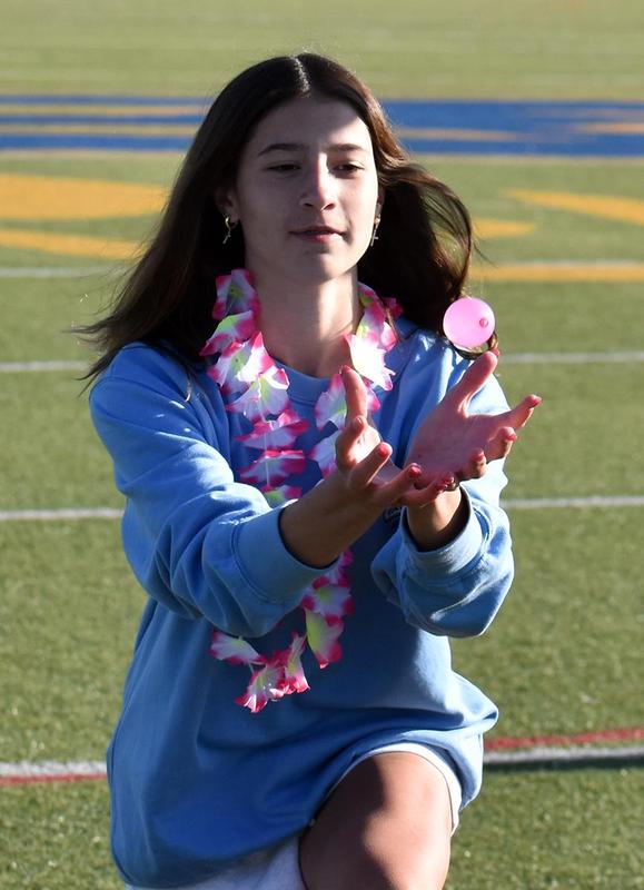 Girl in a light blue sweater, wearing a floral lei, reaches up to catch a balloon.