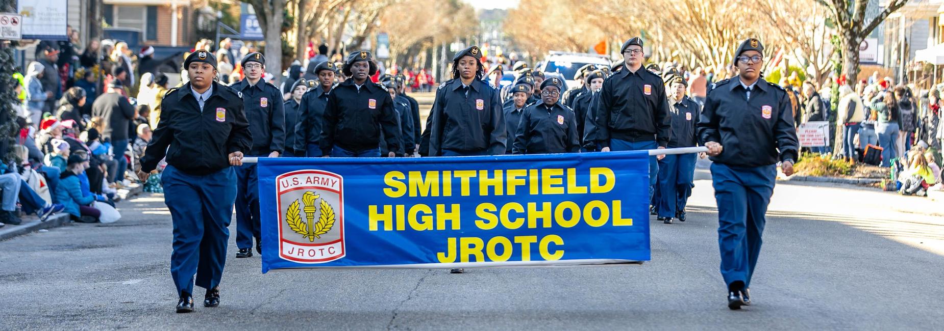 Smithfield High School JROTC marching in a parade carrying a large banner.