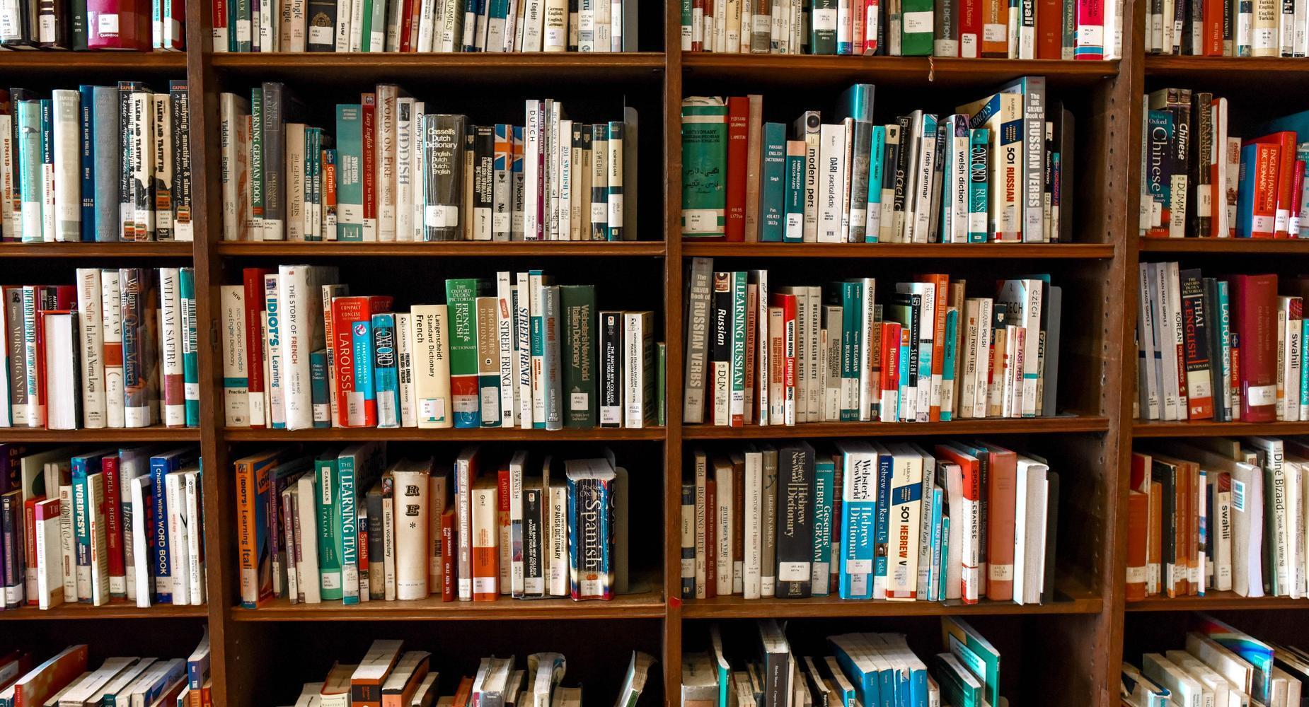 A wooden bookshelf filled with various books organized by color and size.