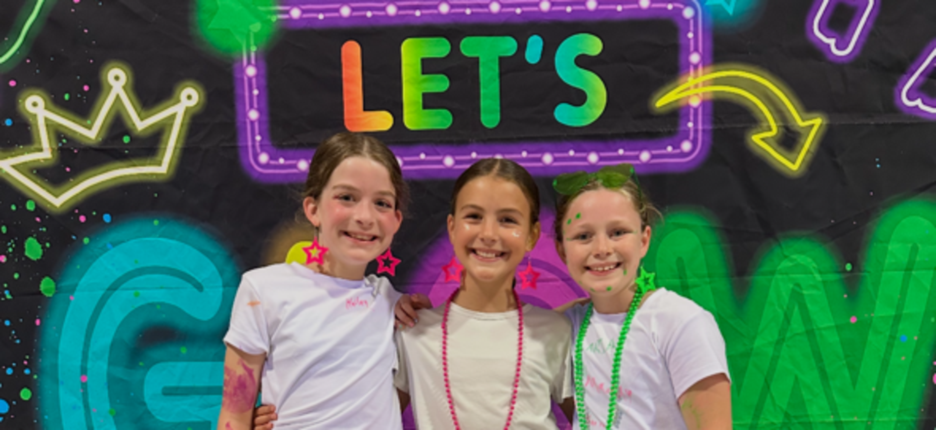 Three children wearing bright tutus and neon accessories against a colorful backdrop.