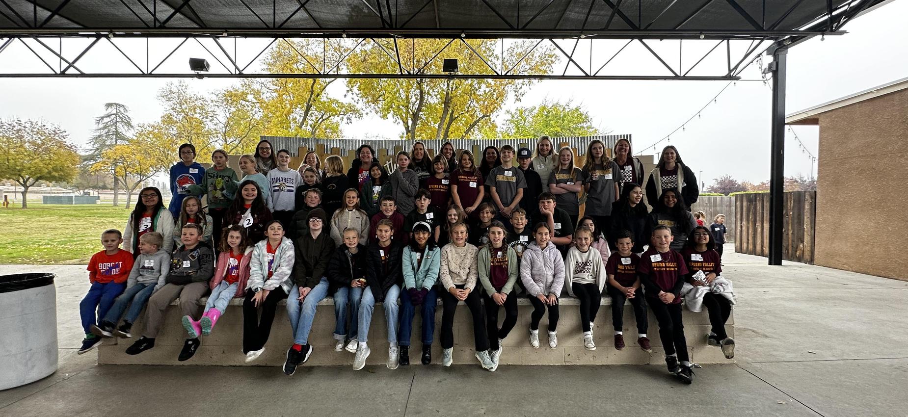 Group of children and adults posing together on a stage outdoors.