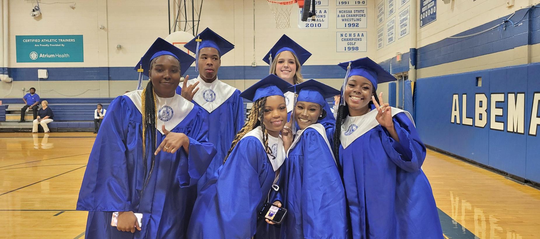 Group of graduates smiling and posing together in blue gowns.