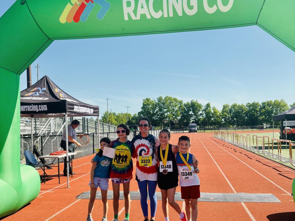 Mrs. Schlosser standing at the finish line with four elementary students at the annual PCF 5K Run/Family Fun Walk.