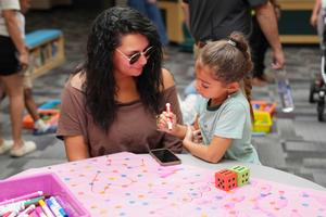 mom watching child drawing on a colorful paper while sitting at table in library
