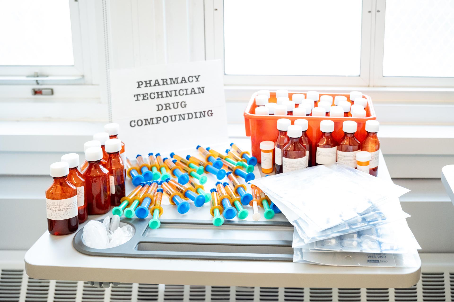 Pharmacy compounding setup with bottles, syringes, and supplies arranged neatly on a table.