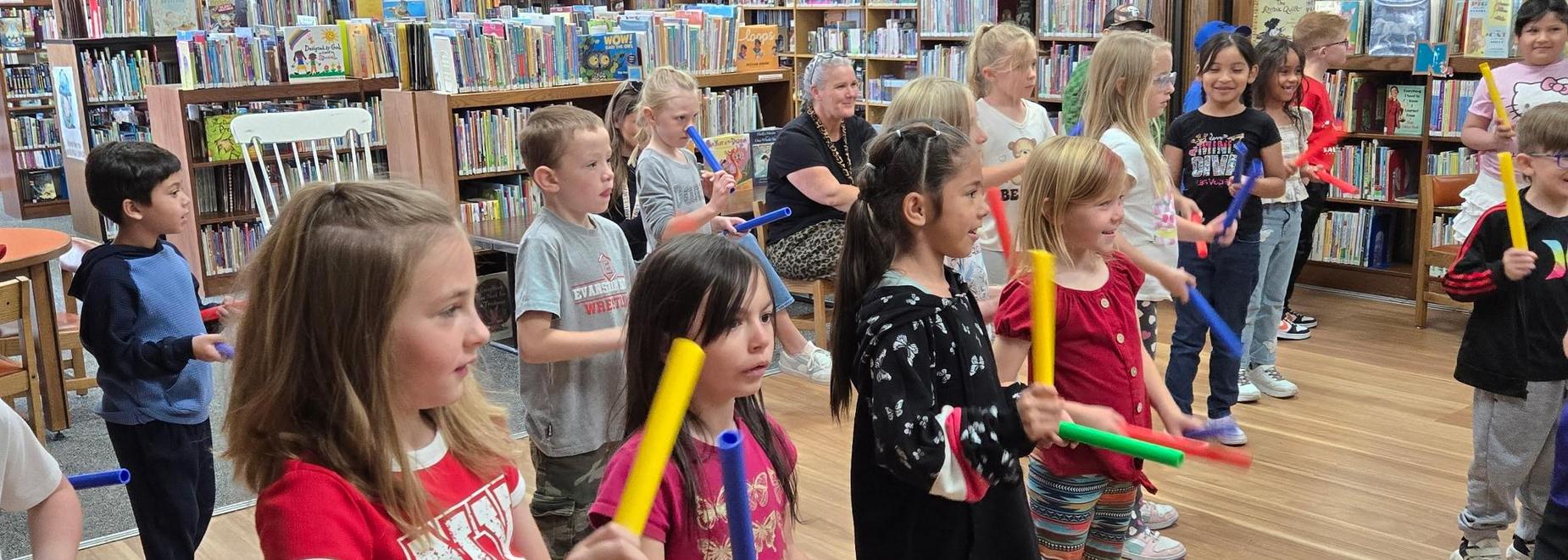 Children holding colorful instruments in a library during a musical activity.