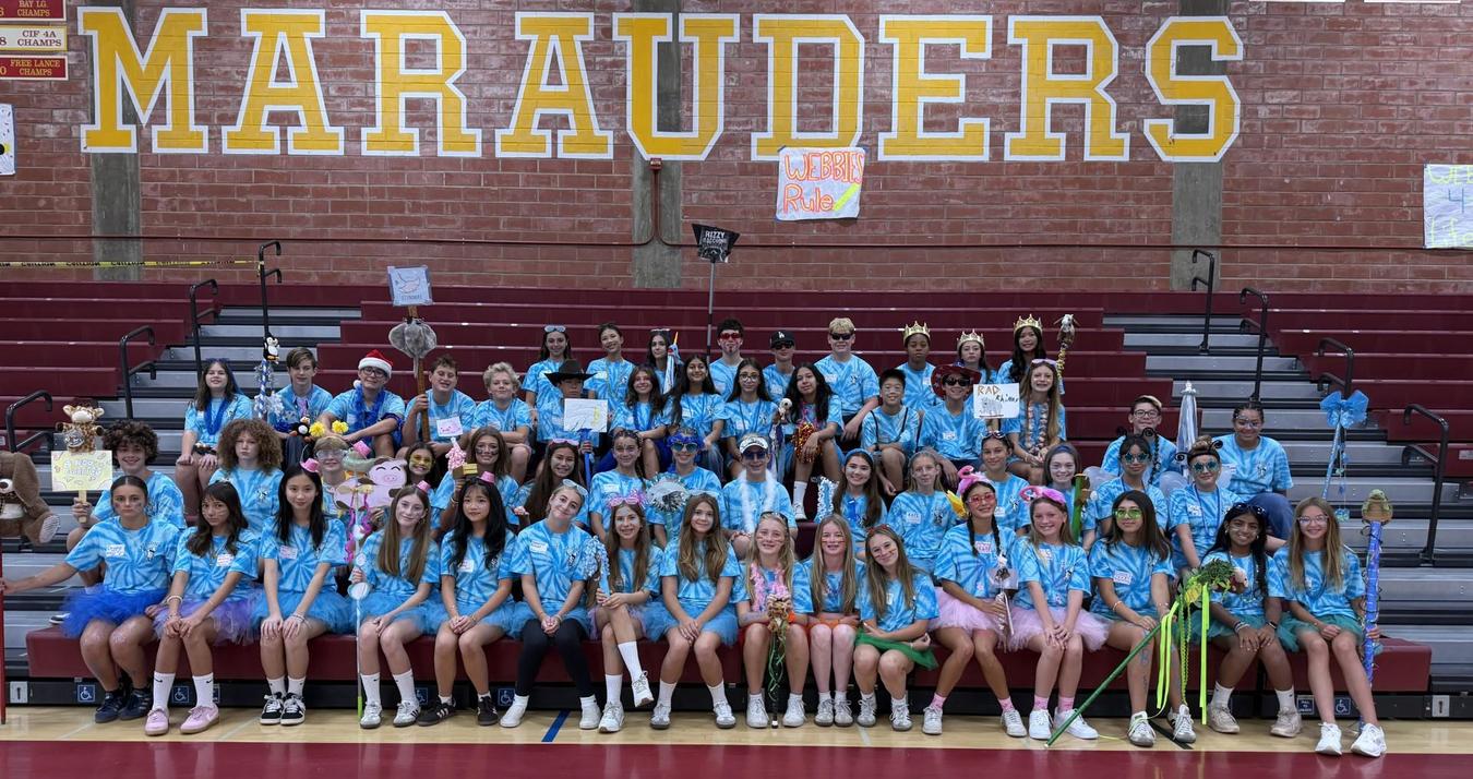 A large group of students in matching outfits poses together in a gym.