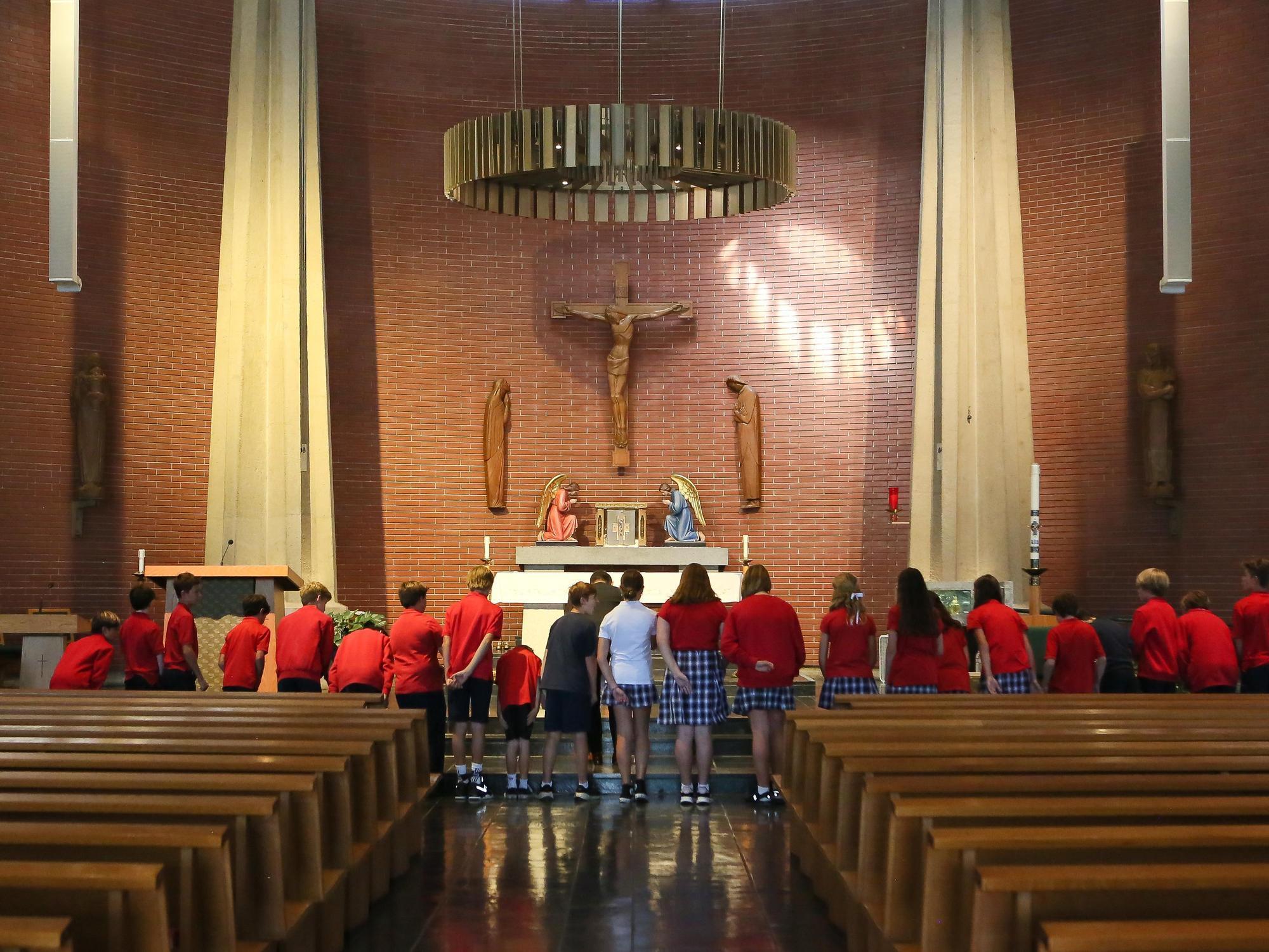 Students in red shirts observing a religious altar inside a chapel.