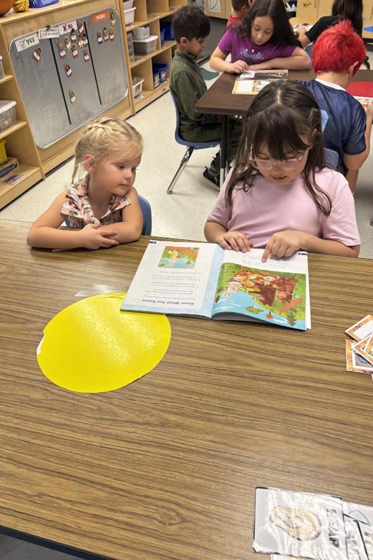 Second grade student reading to preschool student