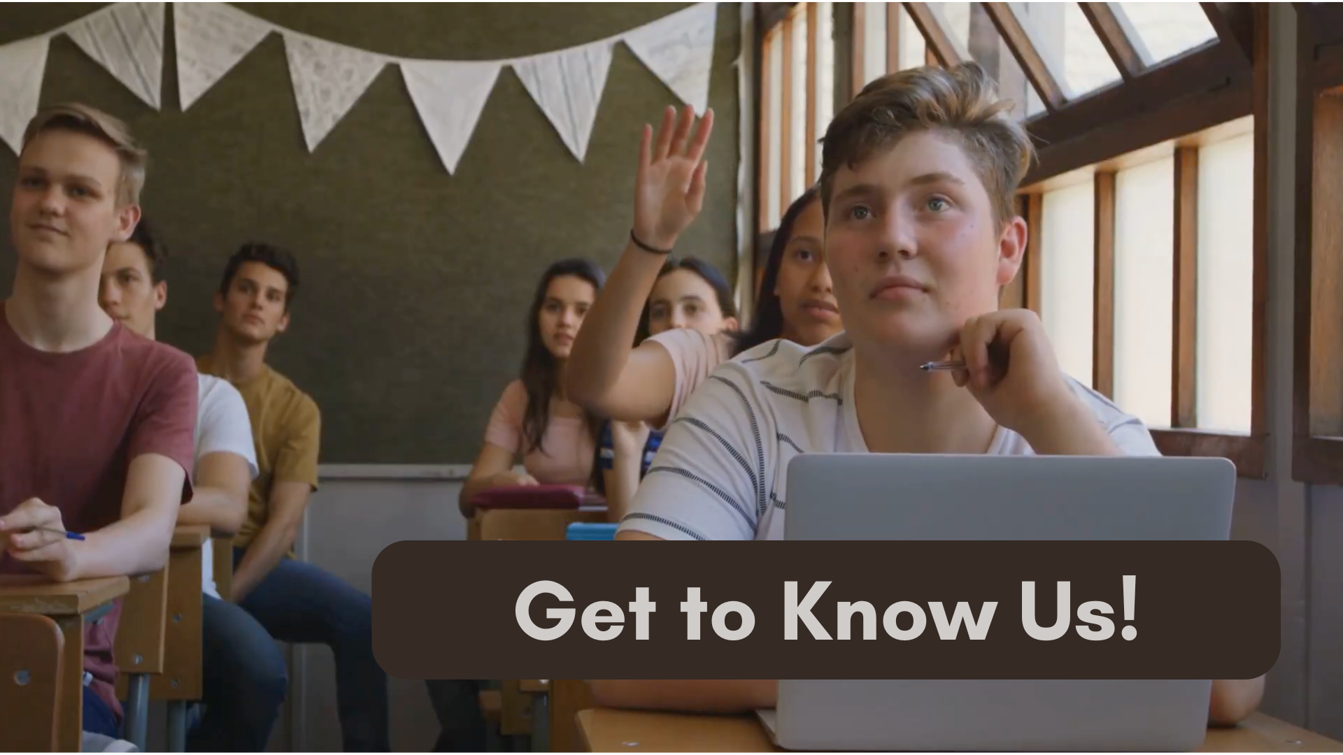 group of students in a classroom all looking to the front of the room with one student raising her hand