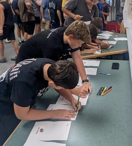 Two Middle School football players sign cards of thanks to donors.