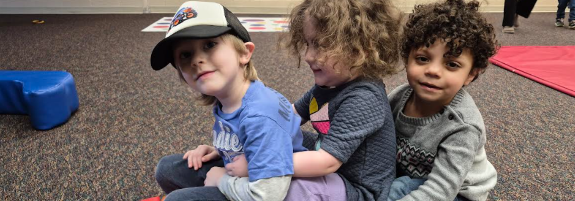 Three children playfully sitting together on a colorful soft toy.